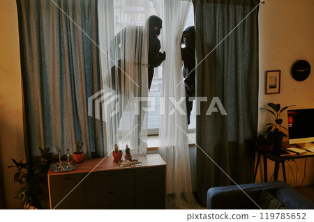 Unrecognizable thieve standing on windowsill and seeing apartment after break-in 119785652