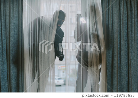 Two unrecognizable thieve in total black clothes looking through white tulle 119785653