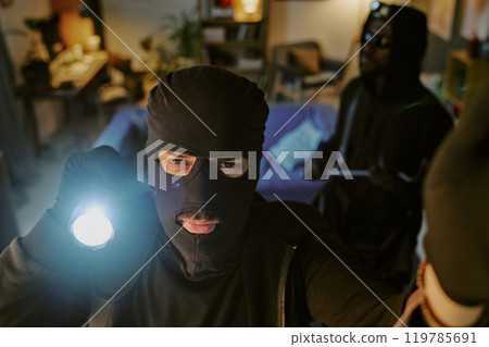High angle shot of thief in black balaclava using flashlight to lookin at camera High angle shot of thief in black balaclava using flashlight to lookin at camera 119785691