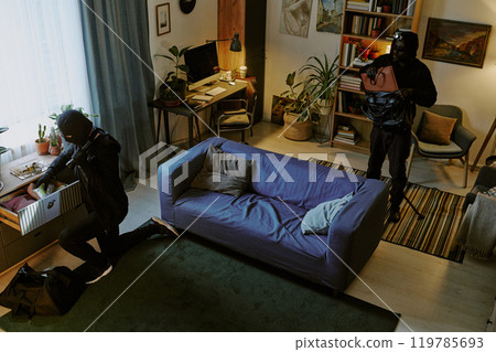 High angle shot of unrecognizable thieve in total back stealing luxury clothes and accessories in living room 119785693