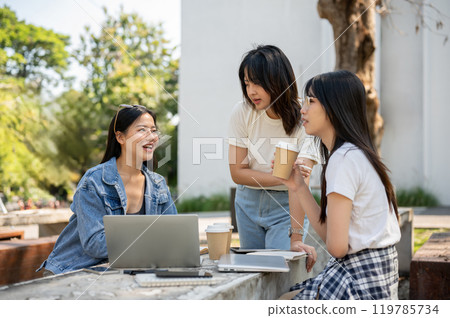 An Asian female college student is discussing work with her friends at a table in a college park. An Asian female college student is discussing work with her friends at a table in a college park. 119785734