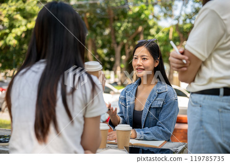 An Asian female college student is discussing work with her friends at a table in a college park. An Asian female college student is discussing work with her friends at a table in a college park. 119785735