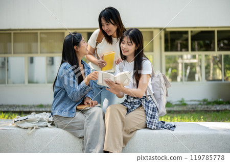 A group of Asian female college students is discussing topics from a book in their college park. A group of Asian female college students is discussing topics from a book in their college park. 119785778
