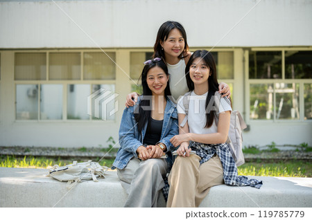 A group of Asian students is sitting on a bench in their college park, smiling at the camera. A group of Asian students is sitting on a bench in their college park, smiling at the camera. 119785779