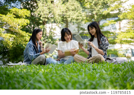 A group of female college students is sitting together on the grass, enjoying reading together. 119785815