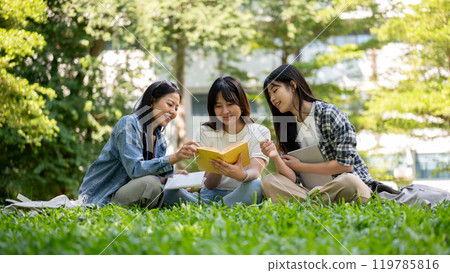 A group of college students sits on the grass in their college campus park, having a conversation. A group of college students sits on the grass in their college campus park, having a conversation. 119785816