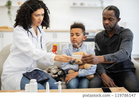 African female doctor giving medicine to sick boy with concerned father 119786147