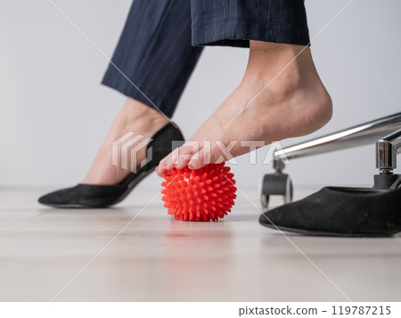 Business woman massages her feet on a massage ball with spikes. 119787215