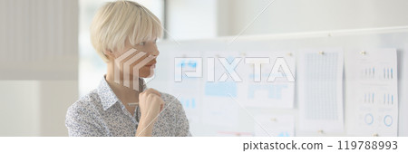 Woman manager thinks looking at diagrams on board in office Woman manager thinks looking at diagrams on board in office 119788993