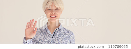 Positive blonde woman in shirt waves hello to camera smiling 119789035