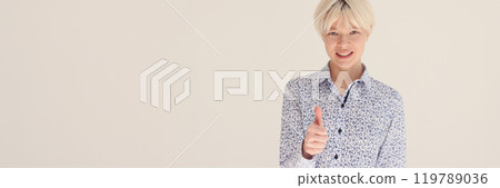Smiling blonde woman shows approval thumb up sign at wall 119789036