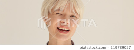 Cheerful blonde woman in shirt winks slyly in light office 119789037
