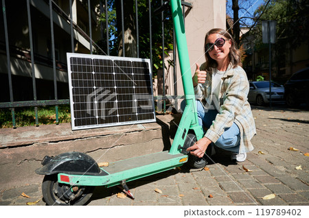 Woman connecting solar panel to electric scooter, highlighting practical application of sustainable renewable energy. Concept of integration of eco-friendly technology in everyday transportation. 119789402