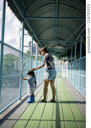 Mother and son looking animal  in an outdoor zoo. They are standing next to a cage with animals. 119791023