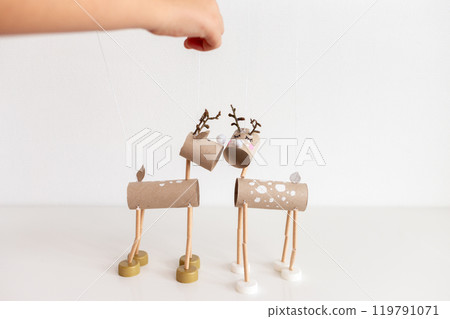 Hand holding wooden stick controlling DIY reindeer puppets crafted from recycle toilet paper roll cardboard tubes and bottle caps. Minimalistic shot for Christmas holiday craft concept. 119791071