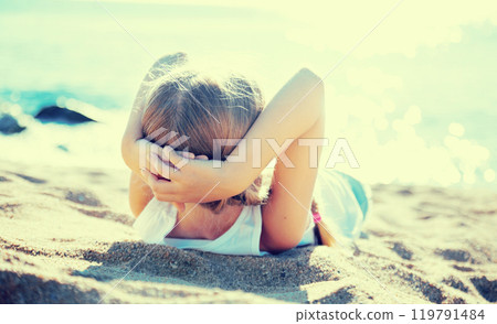 Blond child lying on sandy beach of sea coast 119791484