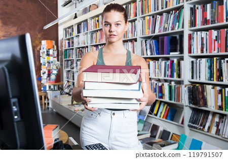 Girl holding a stack of books in a bookstore Girl holding a stack of books in a bookstore 119791507