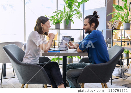 Young man woman sitting at table in coworking space with laptop smartphone, talking together 119791551