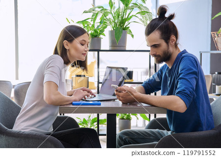 Young man woman sitting at table in coworking space with laptop smartphone, talking together 119791552