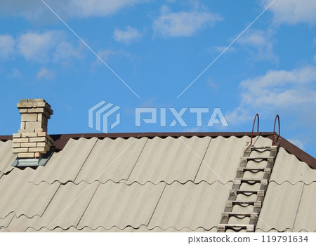 chimney brick pipe and wooden ladder on gray corrugated slate roof of private rural house under clear blue sky, top of rustic building with stairs and kitchen pipe for smoke outlet as country texture chimney brick pipe and wooden ladder on gray corrugated slate roof of private rural house under clear blue sky, top of rustic building with stairs and kitchen pipe for smoke outlet as country texture 119791634