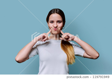 Funny grimacing young teenage woman on blue studio background Funny grimacing young teenage woman on blue studio background 119791949