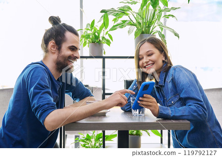 Young man woman sitting together in cafe coffee shop, talking, looking at smartphone 119792127
