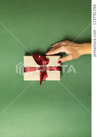 a female hand with a burgundy manicure holds a gift box with a burgundy bow a female hand with a burgundy manicure holds a gift box with a burgundy bow 119792398