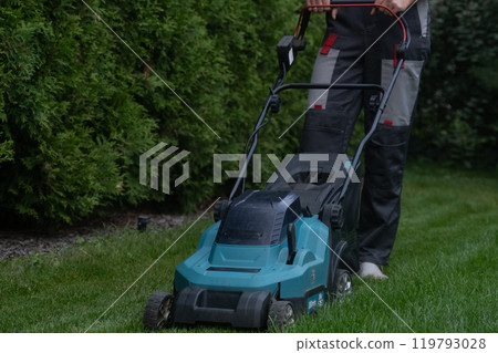 Gardener actively mowing the lawn with a cordless rotary mower 119793028
