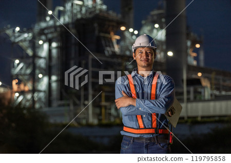 portrait of asian man engineer working at nighttime standing at front of Oil-fired power plant. Worker wear uniform helmet working tower power plant construction. 119795858
