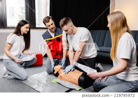 Young man instructor helping to make first aid heart compressions with dummy during the group training indoors Young man instructor helping to make first aid heart compressions with dummy during the group training indoors 119795972