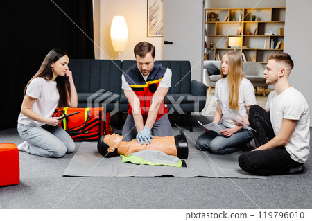 Young man instructor helping to make first aid heart compressions with dummy during the group training indoors Young man instructor helping to make first aid heart compressions with dummy during the group training indoors 119796010