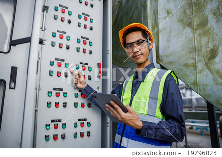 Electrical engineer man using tablet checks switchboard main Distribution Boards control panel electric factory building. Male Industrial technician worker working power distribution room. 119796023