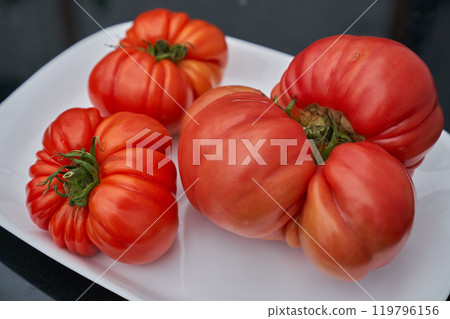 Red tomatoes on the white plate, black table background Red tomatoes on the white plate, black table background 119796156