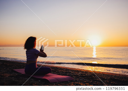 Carefree woman yoga practicing by the sea sunrise time 119796331