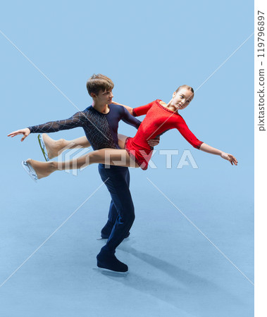Dynamic photo of two figure skaters perform an elegant lift against cold blue background, illustrating strength and grace of competitive skating. 119796897