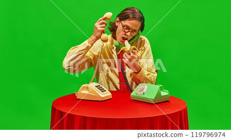 Man stares at banana while talking on two vintage phones, adding quirky and humorous twist to office scene. 119796974