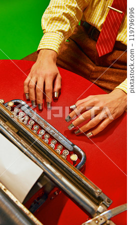 Aerial view of hands near vintage typewriter, fingers with metal thimbles, showing act of typing in retro office environment. 119796996