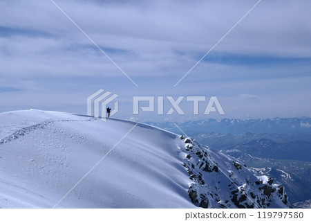 Adventurous hiker enjoying the breathtaking view from a snowy mountain peak 119797580