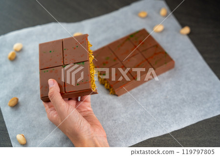 Trend Dubai chocolate with pistachio paste and kataifi dough in woman hands. Confectionery handmade sweets at home in the kitchen. Trend Dubai chocolate with pistachio paste and kataifi dough in woman hands. Confectionery handmade sweets at home in the kitchen. 119797805