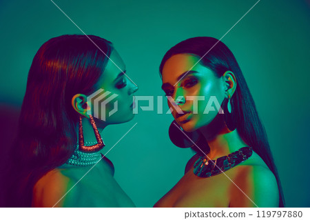 Glamorous portrait of two young beautiful women facing each other, captured in contrasting green and orange lighting. Glamorous portrait of two young beautiful women facing each other, captured in contrasting green and orange lighting. 119797880