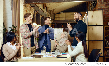 Colleagues from various cultural backgrounds applaud one another around conference table, showing appreciation and encouragement Colleagues from various cultural backgrounds applaud one another around conference table, showing appreciation and encouragement 119797907