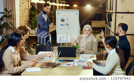 Diverse group of young professionals gathered around table, discussing and working together on project. 119797943