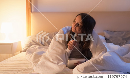 Kid hobby. Night home leisure. Talent art. Inspired pensive small girl thinking before sleep lying in bed late in home bedroom with warm lamp light. 119797974