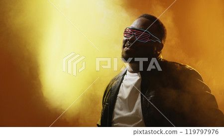 Cyberpunk party. Nightlife leisure. Cool stylish man in trendy futuristic glasses enjoying neon night club atmosphere in glowing light on smoke effect background. Cyberpunk party. Nightlife leisure. Cool stylish man in trendy futuristic glasses enjoying neon night club atmosphere in glowing light on smoke effect background. 119797976