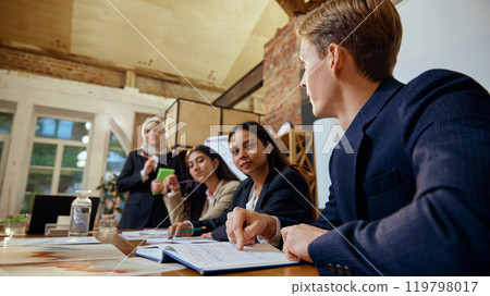 Business professionals engaged in a strategic planning session. Focus on young man in blue suit talking to team, presenting ideas 119798017