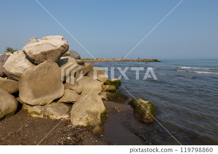 Large rocks on the shore of the Caspian Sea. In the background fishermen stand on the shore and fish with a rod. Large rocks on the shore of the Caspian Sea. In the background fishermen stand on the shore and fish with a rod. 119798860