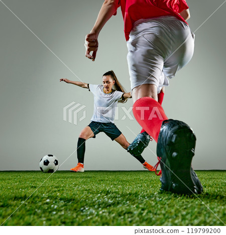 Two female soccer players focused on gaining possession of ball. Women wet after rainy outdoors training. 119799200