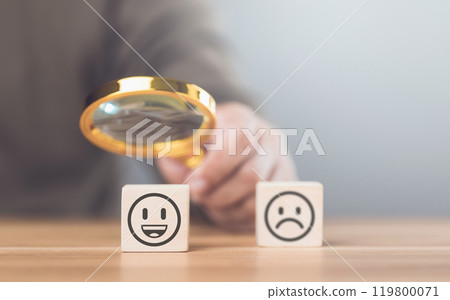 A man choosing between a happy and sad face on wooden blocks, ultimately selecting the happy one. The concept of starting each day with positivity, emphasizing the importance of a bright outlook 119800071