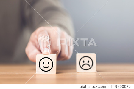 A man choosing between a happy and sad face on wooden blocks, ultimately selecting the happy one. The concept of starting each day with positivity, emphasizing the importance of a bright outlook 119800072