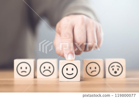 A man choosing between a happy and sad face on wooden blocks, ultimately selecting the happy one. The concept of starting each day with positivity, emphasizing the importance of a bright outlook 119800077